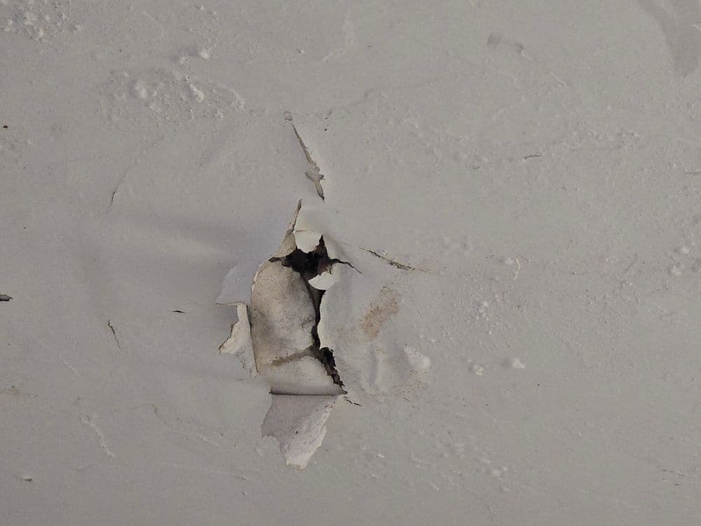 Damage on a wall with peeling paint and a visible hole, indicating wear and tear.