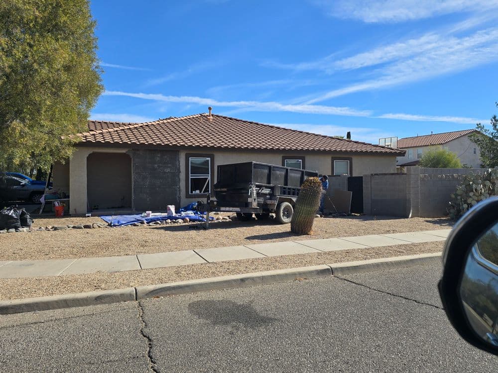 House exterior with a truck, yard debris, and construction materials on a sunny day.