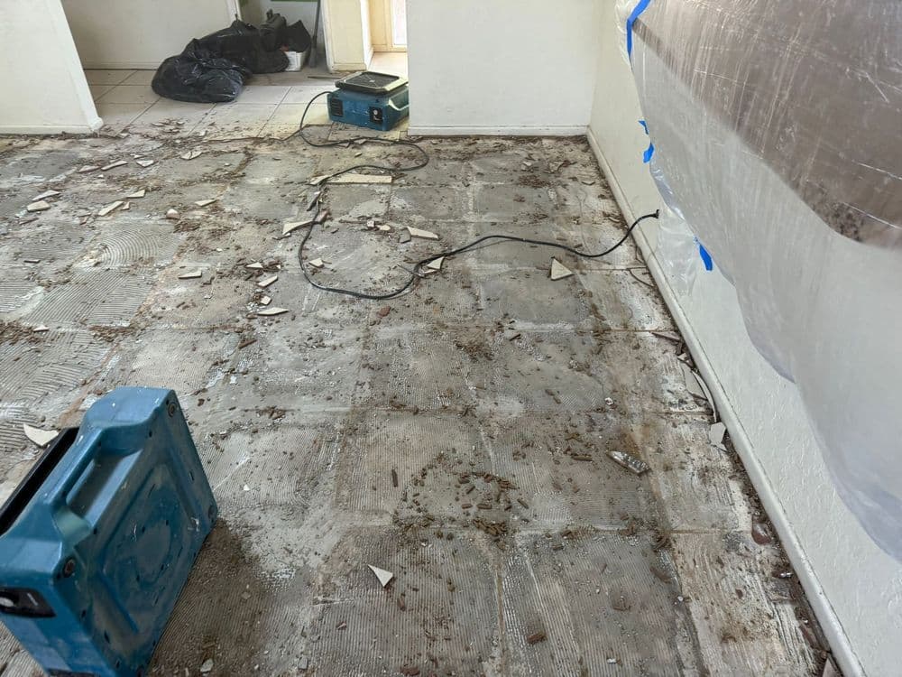 Renovation site with debris and tools on the floor, showing unfinished flooring and cleanup needed.
