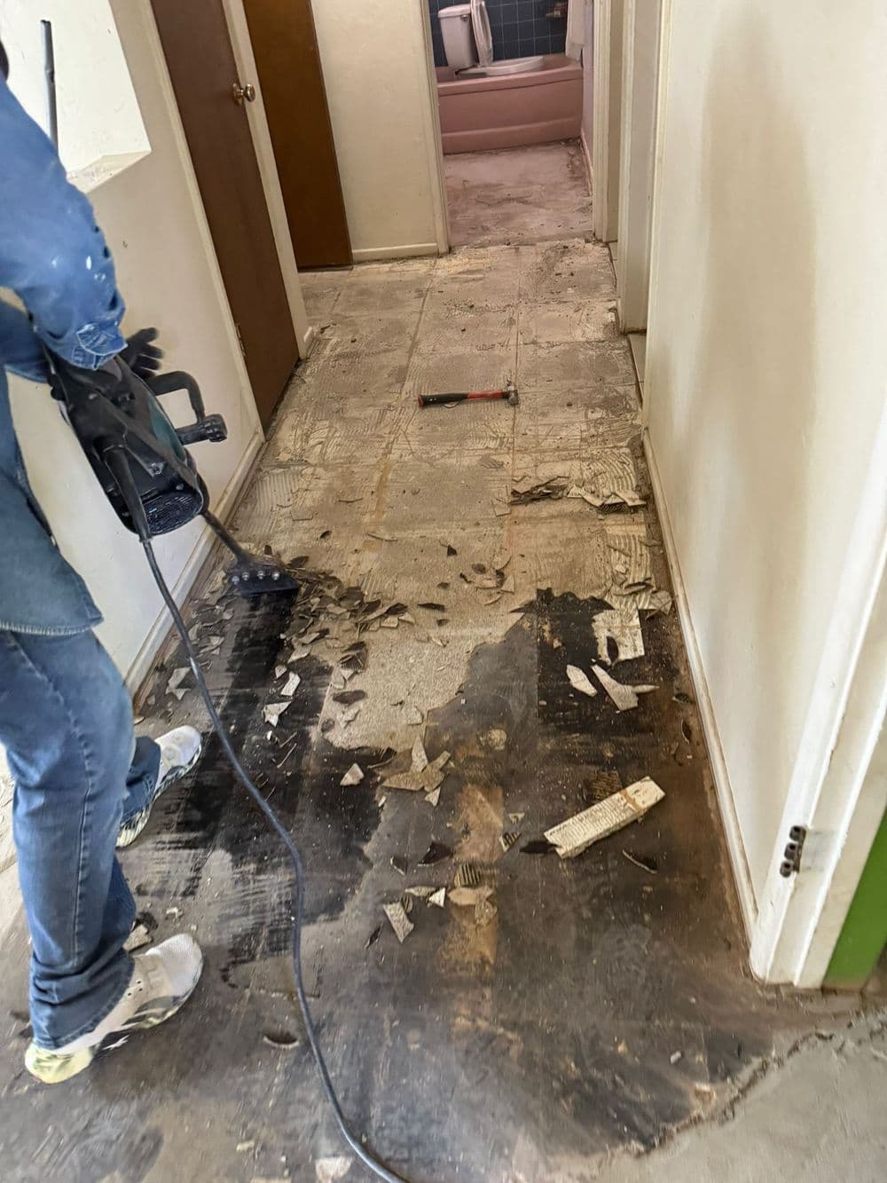Person using a scraper to remove old flooring in a damaged hallway renovation project.