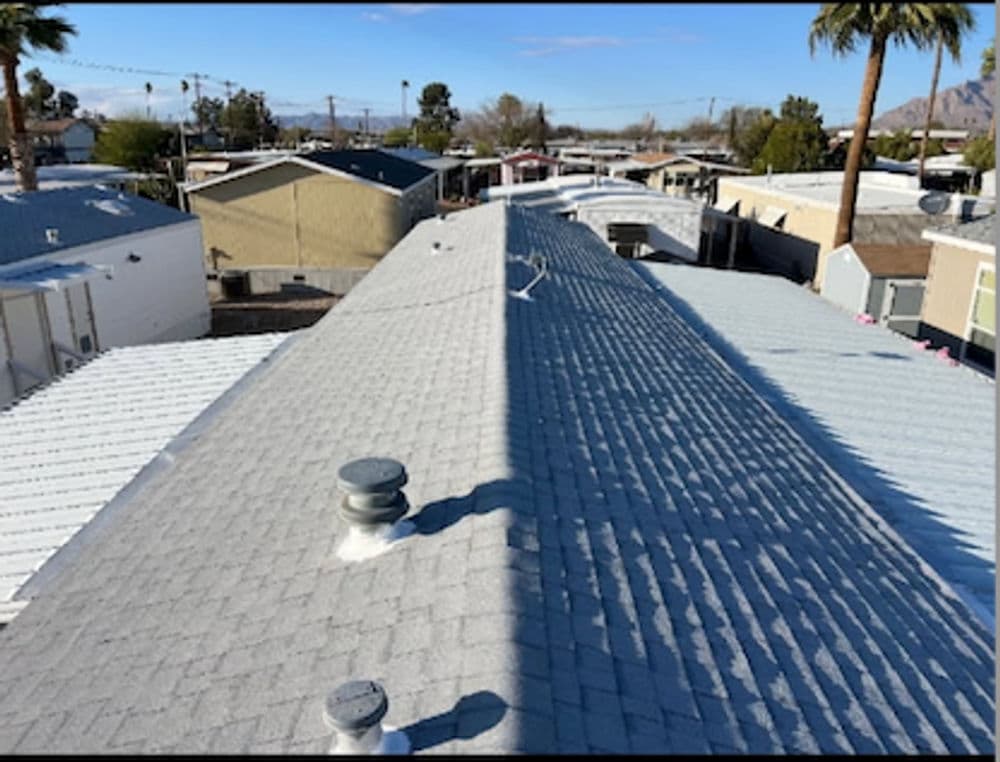 Aerial view of gray roofs in a mobile home community with palm trees and mountains.