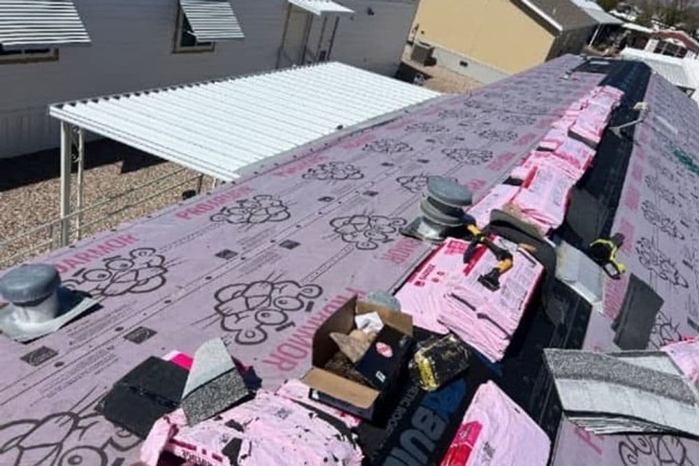 Roofing installation with pink underlayment and ventilation pipes on a residential building.